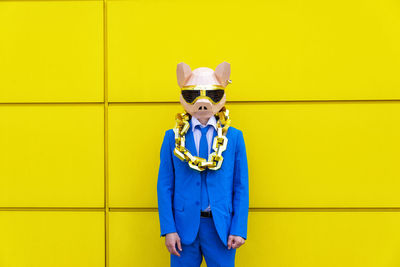 Portrait of person wearing mask standing against yellow wall