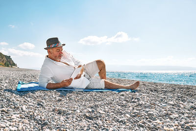 Middle-aged bearded man resting on beach and reading ebook on electronic tablet. concept of reading