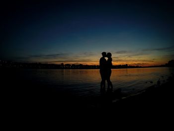 Silhouette couple kissing at lakeshore during sunset