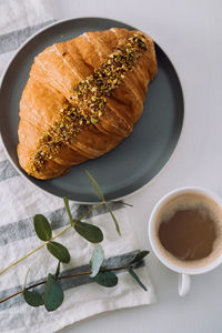 Flat lay of cup of cappuccino with kitchen towel, croissant and eucalyptus branch on the table	
