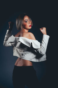 Rear view of seductive woman wearing jacket standing against black background