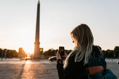 Rear view of woman using phone against sky during sunset