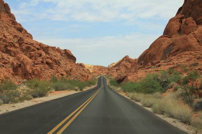 Empty road amidst mountains against cloudy sky