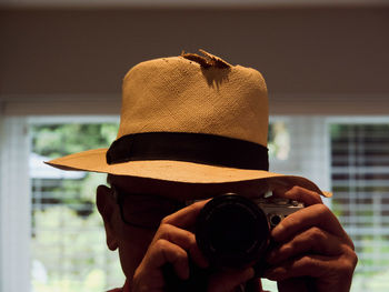 Close-up of man wearing hat while photographing with camera at home