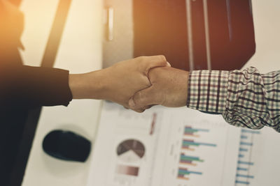 Midsection of colleagues handshaking over office desk