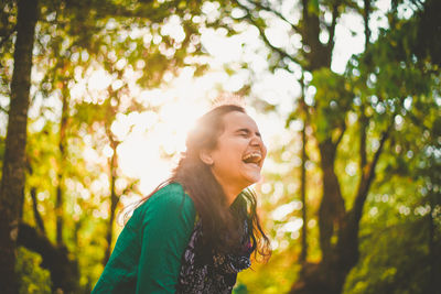 Smiling young woman looking away against trees