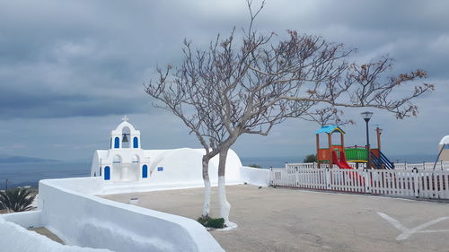 Bare tree by building against sky during winter