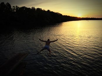 Silhouette man jumping in lake against sky during sunset