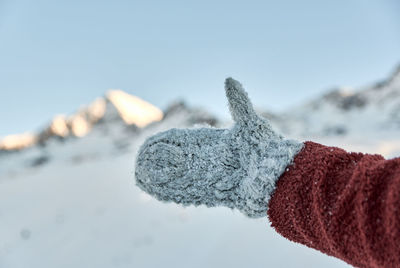 Close-up of hand on snow against sky