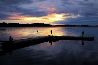 Silhouette people on lake against sky during sunset