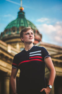 Young man looking away while standing against sky