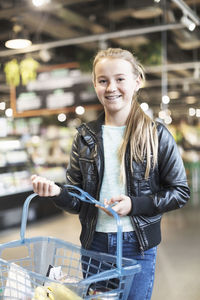 Portrait of smiling girl carrying basket in organic grocery store