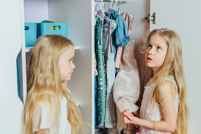 Two little beautiful girls friends sisters play fashion, choose outfits, clothes from a white