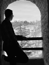 Side view of young man looking through window