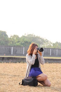 Woman photographing while kneeling on field
