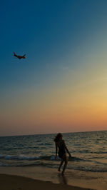 Silhouette woman walking at beach during sunset