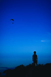 A silhouette boy looking at a blurred silhouette parachute with the dark blue background