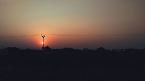 Silhouette electricity pylons against sky at sunset