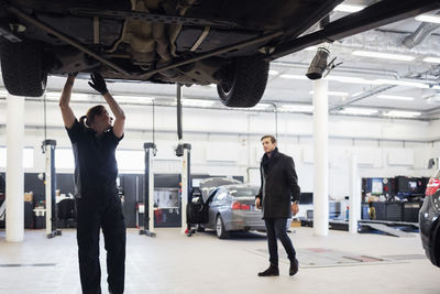 Mechanic looking at customer while working under car at repair shop