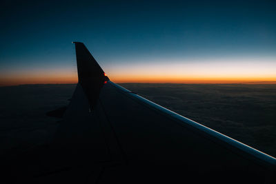 Airplane flying over landscape against sky during sunset