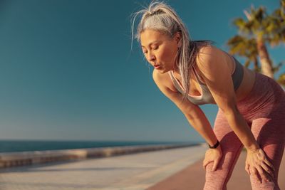 Side view of young woman exercising on beach against sky