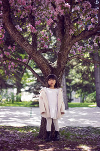 Korean girl in a white light fur coat and a headband stands in a garden with cherry blossoms