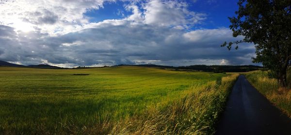 Panoramic shot of road amidst field against sky