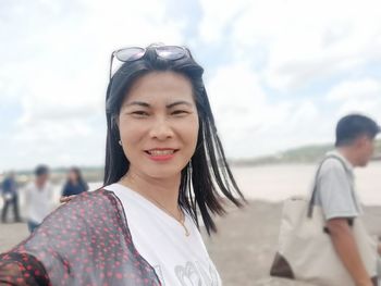 Portrait of smiling young woman on beach against sky