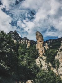 Low angle view of rocky mountains against cloudy sky