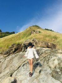 Rear view of woman standing on rock against sky