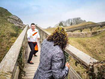 Happy couple enjoying on footbridge against sky