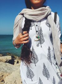 Midsection of woman wearing salwar kameez standing on rocks by sea against sky