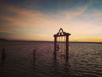 Silhouette wooden post in sea against sky during sunset