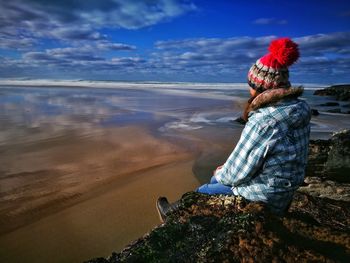 Full length of woman sitting on cliff at beach against sky