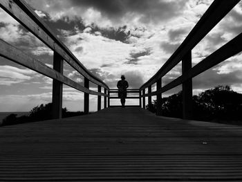 Man standing on footbridge against sky