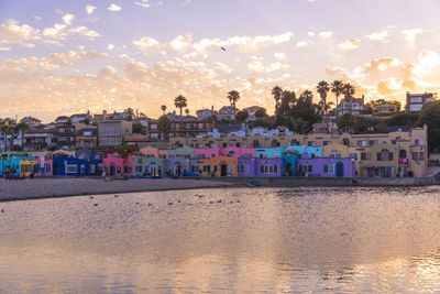 Buildings by sea against sky during sunset