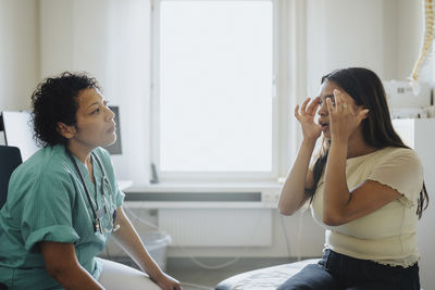 Young woman touching head while discussing with female physician in clinic