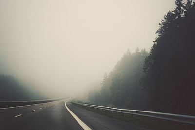 Road by trees against sky during foggy weather