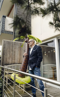 Senior businessman standing in his garden, holding a rubber palm, dreaming of vacations