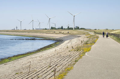 Wind turbines on footpath by road against sky