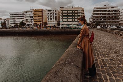 Woman standing in front of buildings against sky in city