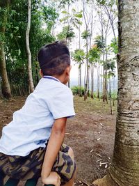 Side view of boy wearing sunglasses on tree trunk