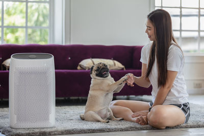 Full length of woman holding paw of dog sitting at home