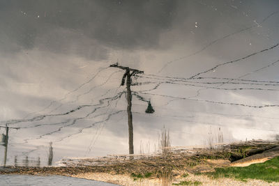 Low angle water reflection view of electric pole on field against sky