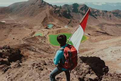 Rear view of hiker holding flag on mountain