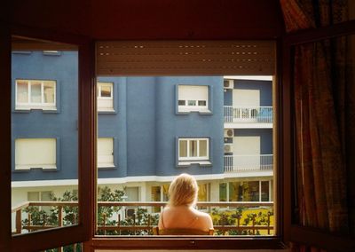 Rear view of woman sitting on chair in balcony against building