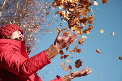 Low angle view of person by autumn leaves against sky