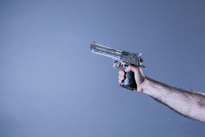 Cropped hand of man holding gun against blue background