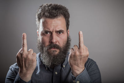 Portrait of bearded man showing middle fingers against gray background