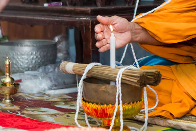 Midsection of monk sitting by candle during religious ceremony